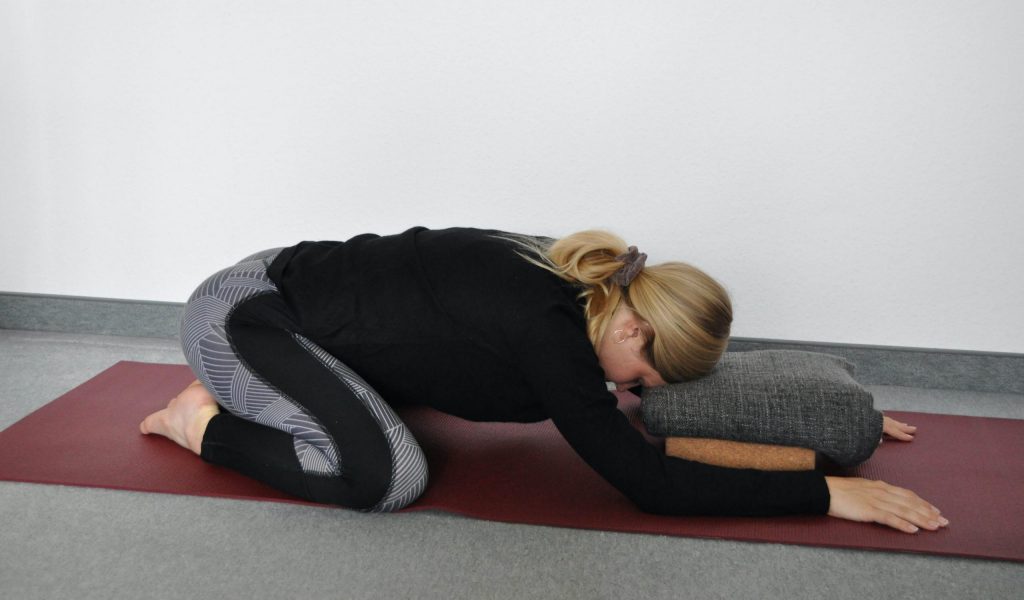 Child's pose variation with arms beside body
